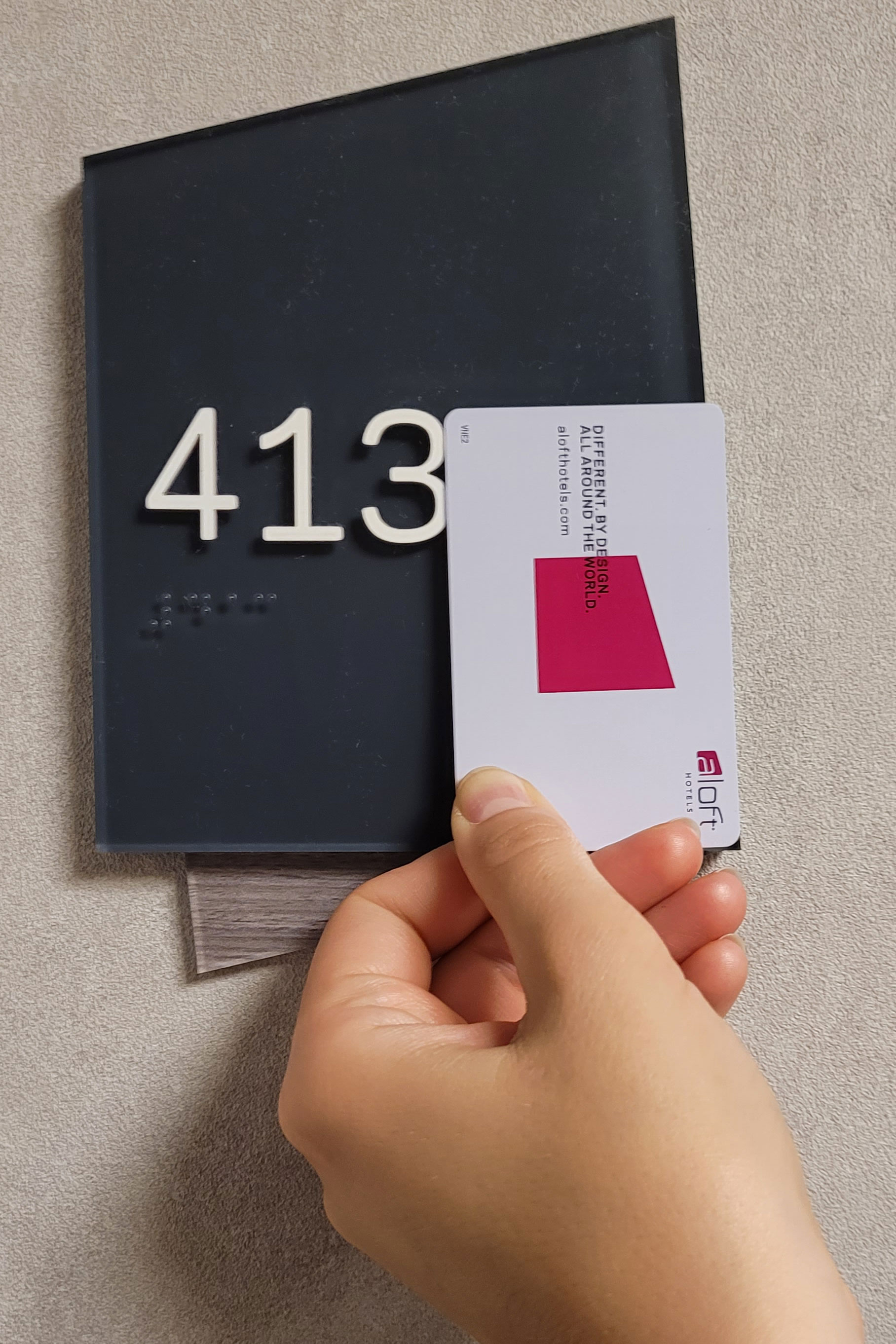 Dłoń trzymająca kartę hotelową na tle tabliczki informacyjnej