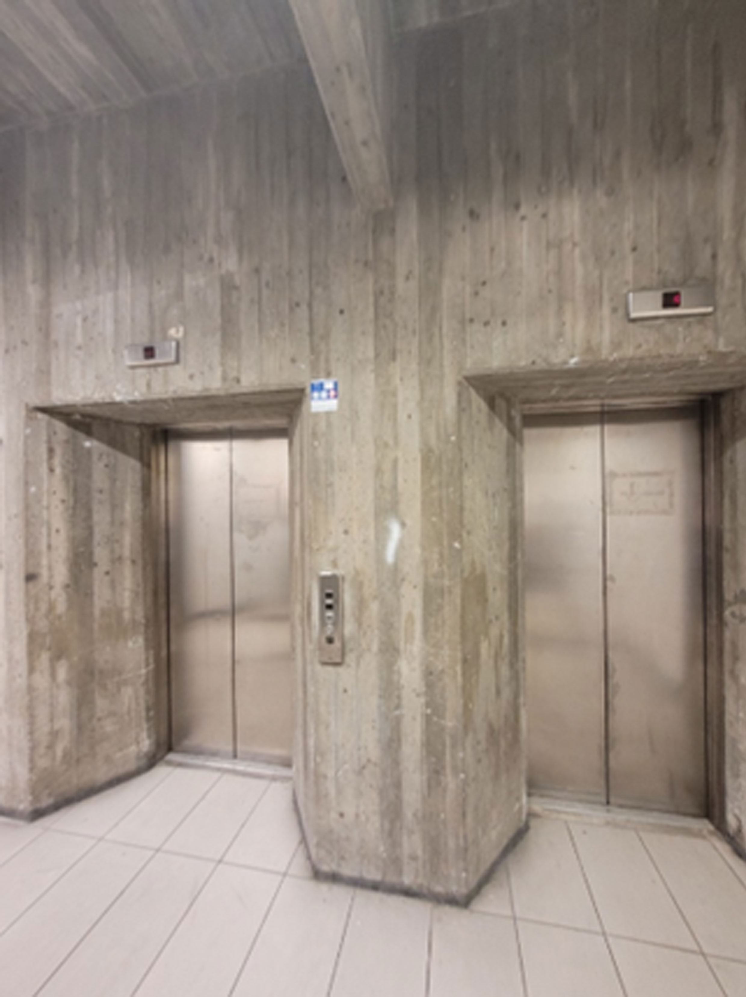stalowe windy w nowoczesnym budynku, którego ściany wykończone są deskowaniem odbitym w surowym betonie