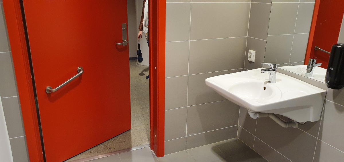 Zdjęcie przedsionka toalety. Kontrastujące drzwi, z antabą; umywalka dostosowana bez pochwytów 