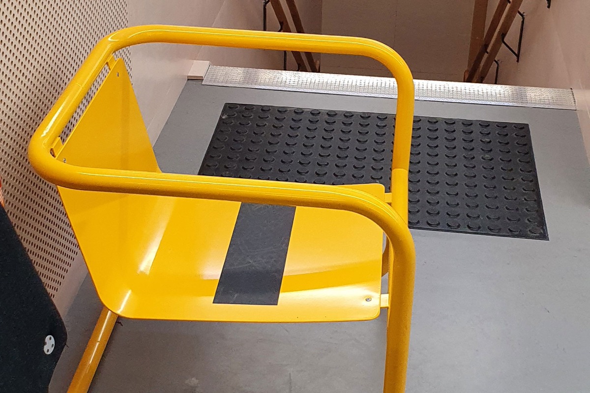 Na holu przy schodach ustawiono żółte, metalowe krzesło mogące służyć do ewakuacji 